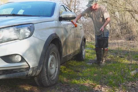 Man in a cap washes the car with a sponge and water from a bucket Stock Photos