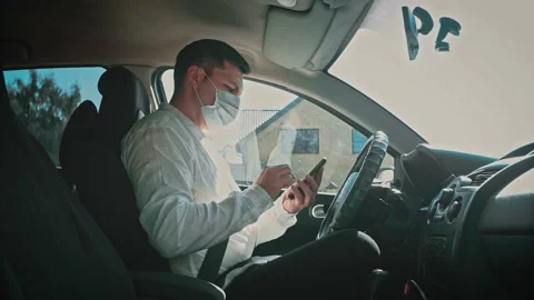 A man in a car in a disposable mask writes messages on the phone. Stock Footage 150154829