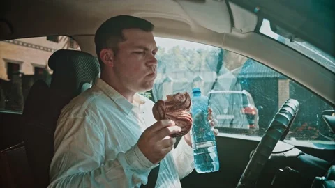 A man in a car in a good mood eats a bun and drinks water. Stock Footage 150156368