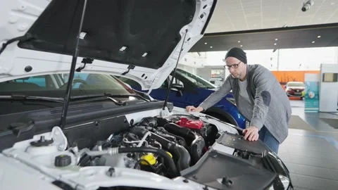 A man in a car showroom examines an engine under the hood. Stock Footage 195735133
