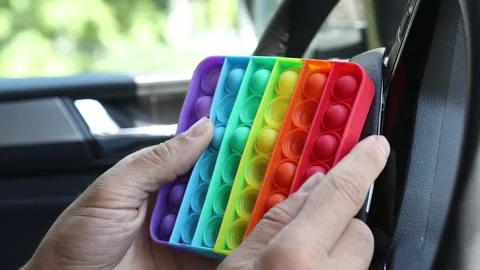 A man in a car standing in a traffic jam relieves stress by playing pop it. Stock Footage 154906102