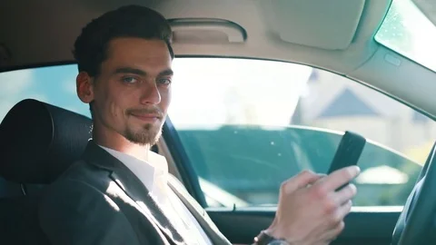 Man in car. Typing text message on mobile phone, looks at camera and smiling Stock Footage 78211644