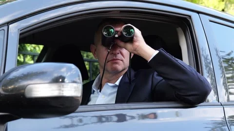 Man in car using binoculars for covert surveillance outdoors Stock Footage 345708389