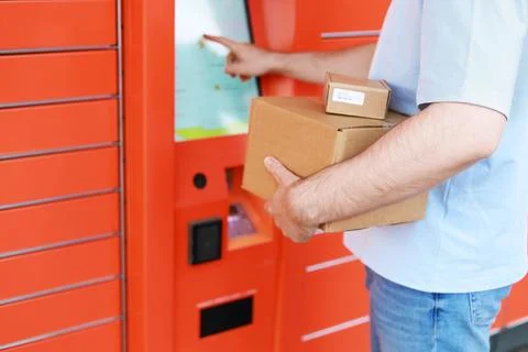 A man with cardboard boxes uses the touchscreen of an automated orange mail.. Stock Photos