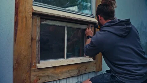 A Man is Carefully Installing the Wooden Frame of a Window on the Exterior of a Stock Footage 336621523
