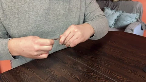 Man carefully trims and files his fingernails at a table. Stock Footage 306530800