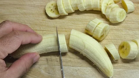 A man carefully uses a kitchen knife to slice a banana into pieces. Stock Footage 318009598