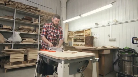Man carpenter with a beard in a shirt with a circular saw on wood in the Stock Footage 88963421