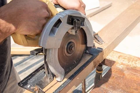 Man carpenter sawing depth setup circular saw wooden beam board on sawhorse Stockfoto's