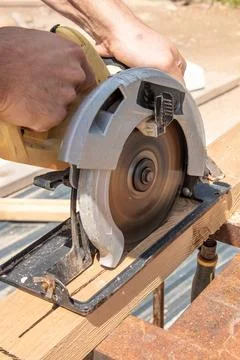 Man carpenter sawing depth setup circular saw wooden beam board on sawhorse Photos