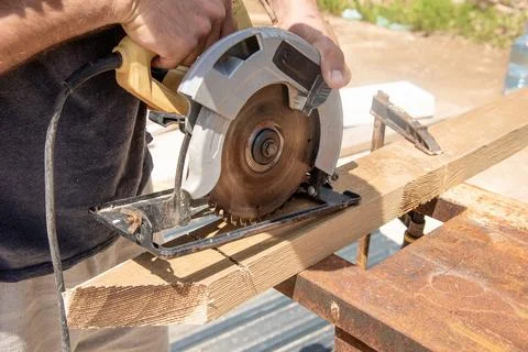 Man carpenter sawing depth setup circular saw wooden beam board on sawhorse Foto stock