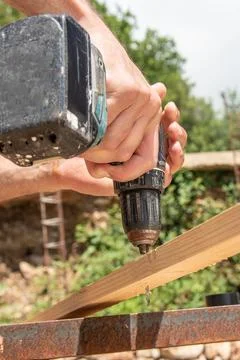 Man Carpenter through drilling Use Cordless Drill In Wooden Board On sawhorse Photos