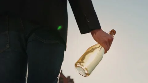 Man carries a bottle of champagne at the setting sun on the roof of a skyscraper Stock Footage 201469318