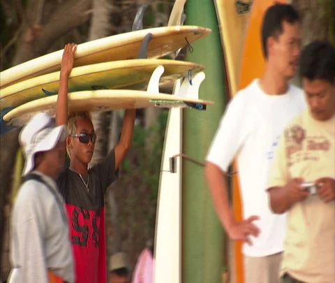 Man carries three surfboards on his head past vendors at beach Stock Footage 86747152