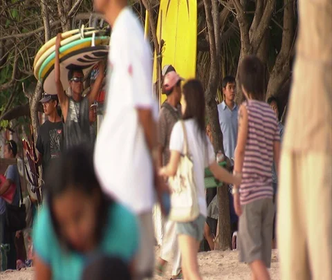 Man carries three surfboards on his head past vendor stalls and crowd at beach Stock Footage 86747162