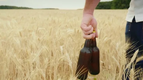 A man carries two bottles of cold beer over a field of barley. The concept is to Stock Footage 77299402