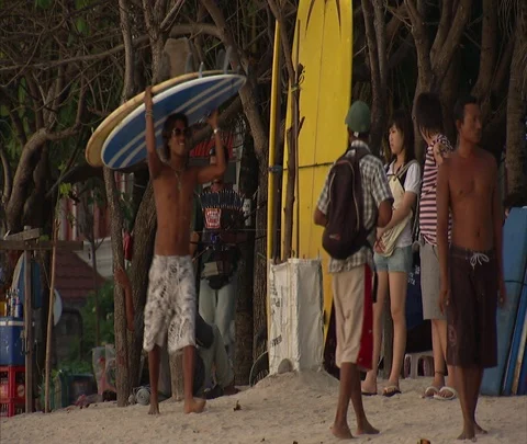 Man carries two surfboards on his head past vendor stalls and crowd at beach Stock Footage 86747205