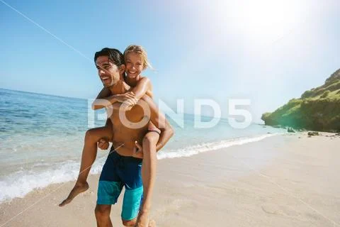 Man Carrying Girlfriend On His Back Along The Sea Shore
