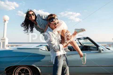 Man carrying his woman and having fun near vintage cabriolet Stock Photos