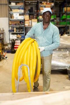 Man carrying rolled corrugated pipe in warehouse Stock Photos