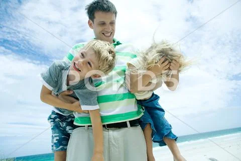 Man Carrying Son And Daughter On Beach