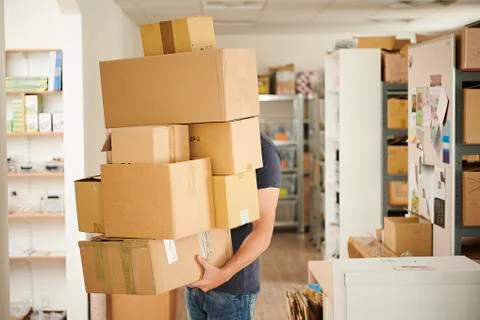A man carrying a stack of boxes across a store room. 스톡 사진