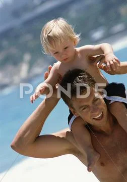 Man Carrying Young Child On Shoulders At The Beach.