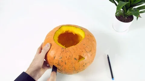 Man carves jack o lantern out of pumpkin on a kitchen table using knife Stock Footage 102557300
