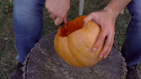Man carves from a pumpkin Jack-o'-lantern in the backyard on a tree stump Stock Footage