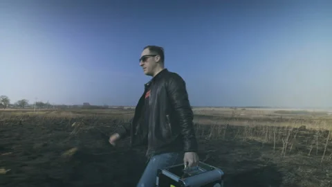 A man with a case is walking along a burning field. Video stock 87919129