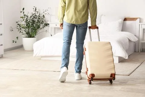 Man in casual attire pulling a suitcase in a modern bedroom, travel and reloc Stock Photos