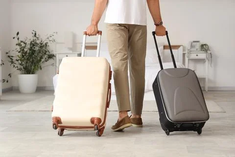 Man in casual attire pulling two suitcases in a bright hotel room, travel and Stock Photos