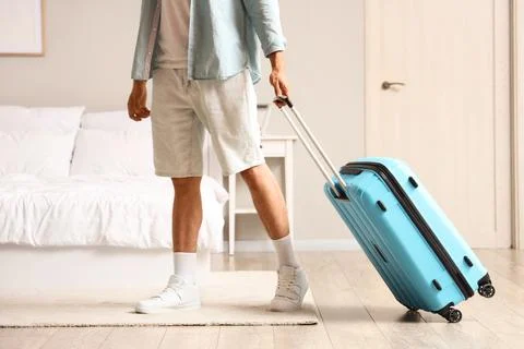 Man in casual summer clothes pulling a blue suitcase on wheels across a bedro Stock Photos