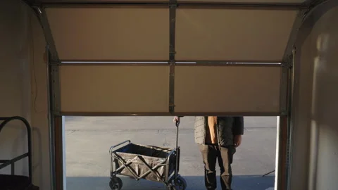 A man casually standing with a wagon in the opening of a garage door during Vídeo Stock 307834754