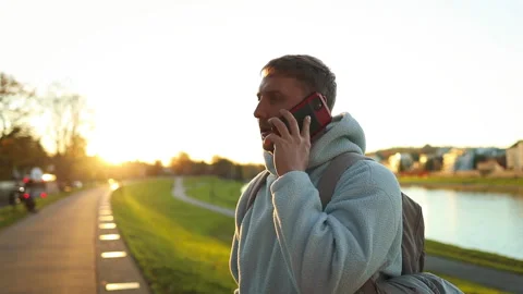 Man casually walking and talking on phone along concrete pathway near water surf Stock Footage 338172062