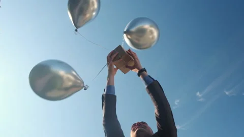 Man catches box attached to helium balloons against blue sky Stockbeeldmateriaal 170483868