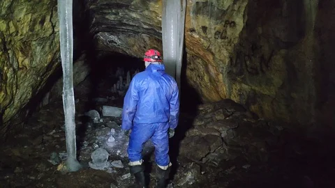 A man in a cave with a flashlight walks between stalactids and stalagmites Stock Footage 129495012