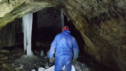 A man in a cave with a flashlight walks between stalactids and stalagmites Stock Footage 129495100