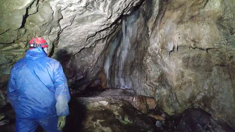 A man in a cave with a flashlight walks through the cave to the ice on the wall Stock Footage 129495014