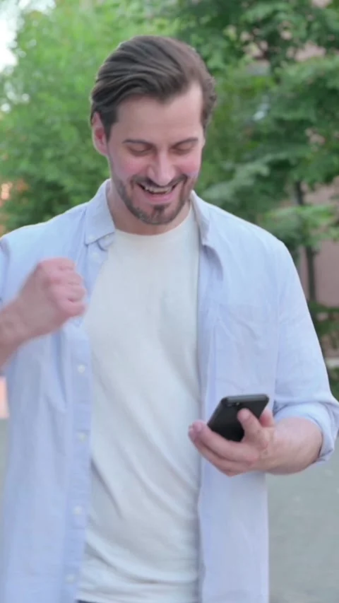 Man Celebrating Success on Phone while Walking in Street, Vertical Video Stock Footage 339666133