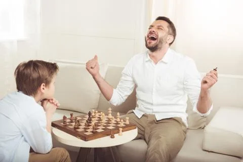 Man celebrating win in chess game with upset son near by 写真素材