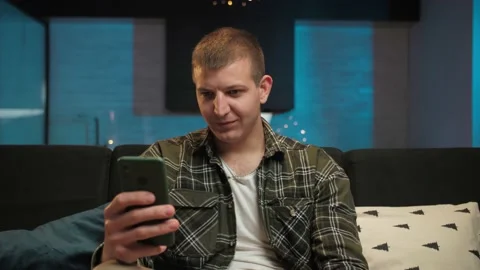 Man celebration victory using phone sitting at couch indoor interior.Young guy Stock Footage 225654435