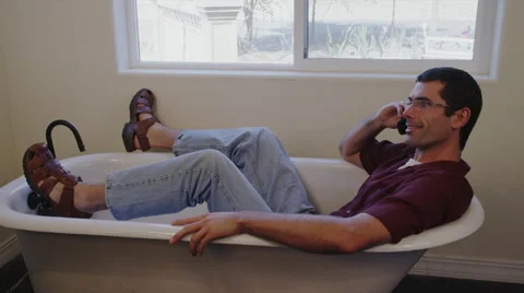 Man on Cell Phone in Empty Bath Tub Wearing Sandals Stock Footage 35296892