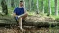 Man with cell phone sits on fallen tree in the forest HD Footage
