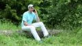 Man with a cell phone sits on a fallen tree in the forest HD Footage