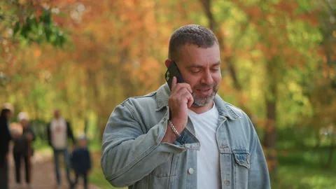 Man on cell phone walking through autumn park with fall foliage background Stock Footage 346722725