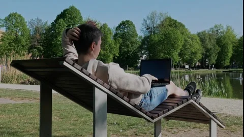 A man in a chaise lounge working on his laptop by the lake. Stock Footage 308398804