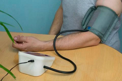 A man changes his pressure by a tonometer sitting at a table with a cuff on h Stock Photos