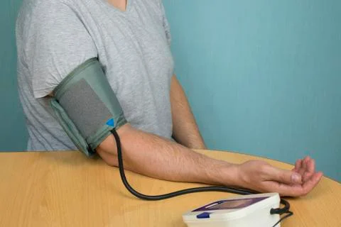 A man changes his pressure by a tonometer sitting at a table with a cuff on h Stock Photos