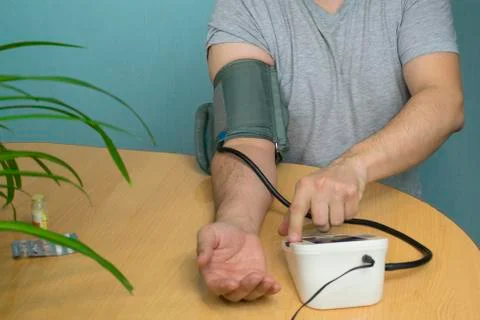 A man changes his pressure by a tonometer sitting at a table with a cuff on h Stock Photos
